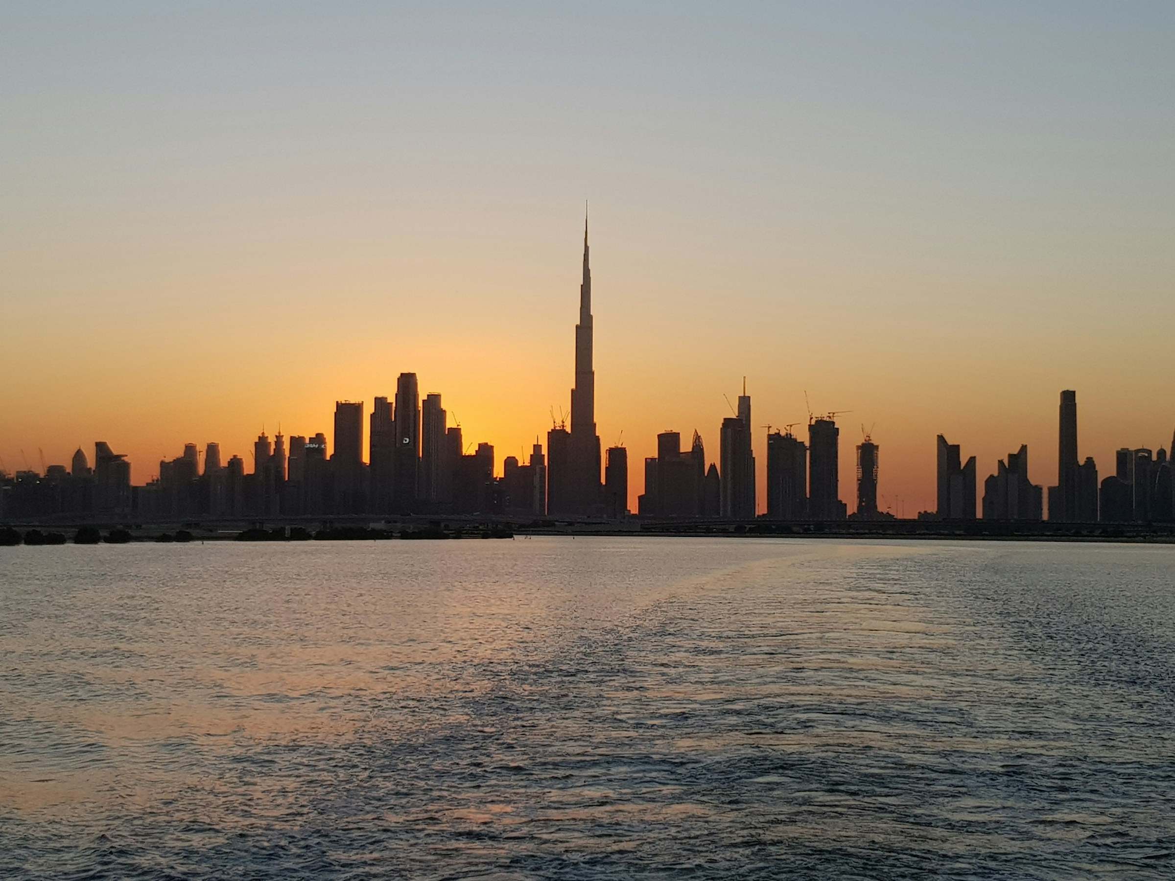 The Dubai skyline in silhouette across the water at sunset